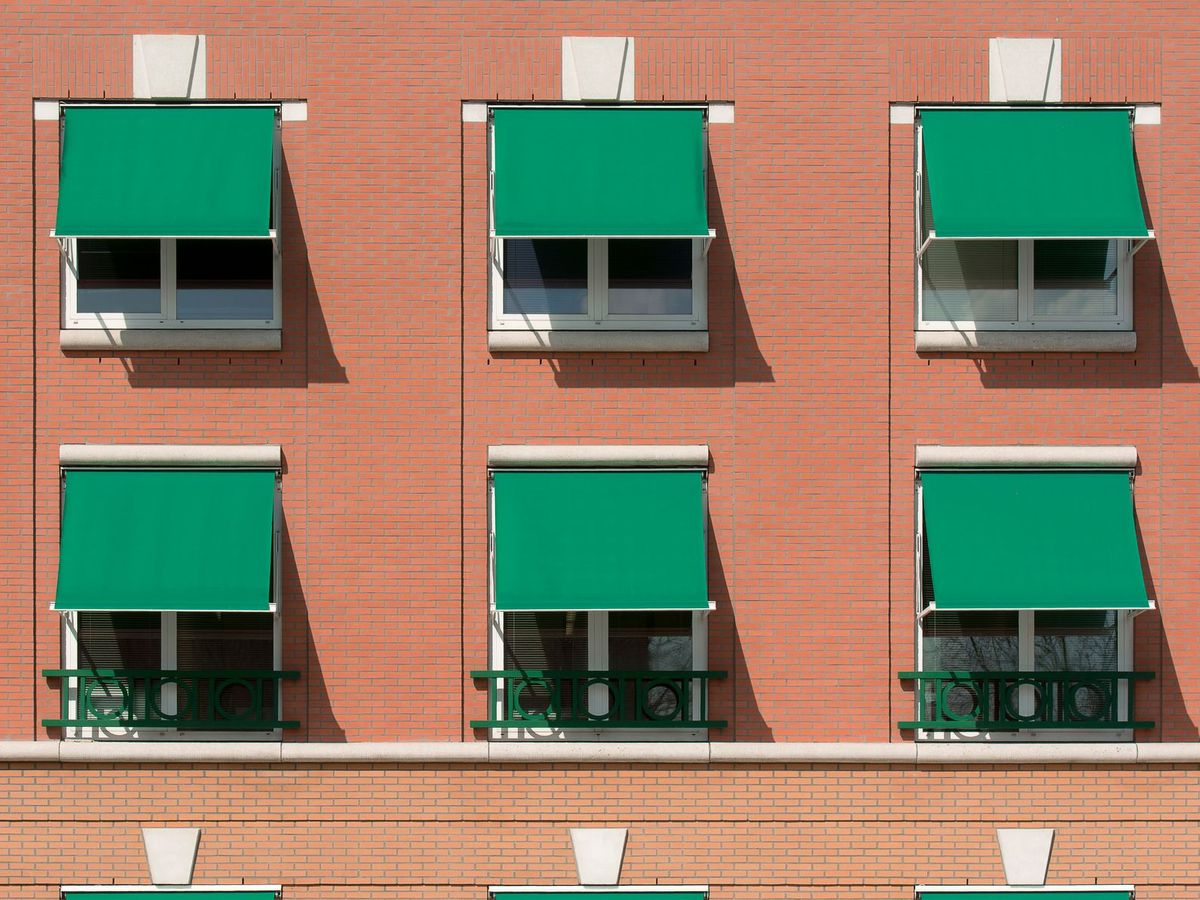 Toldos verdes de punto recto en las ventanas de un edificio de ladrillo